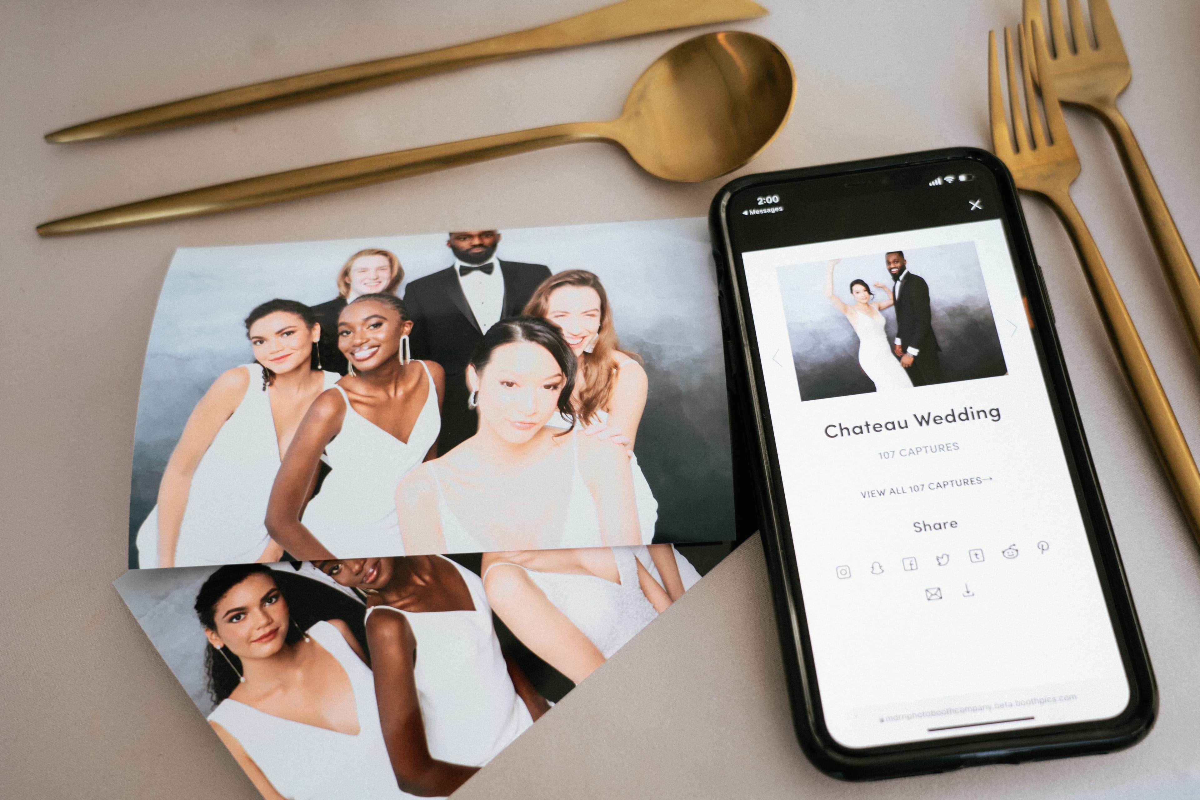 Photo booth prints and digital gallery on a phone next to gold cutlery
